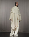 Profile shot of the Nube poncho, showing the draped silhouette and the raw texture of desert wool with fringes. 