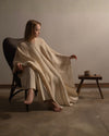Model sitting the long squared silhouette and flud movement of the Silence poncho in a minimalist setting. 