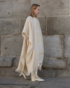 Profile view of model walking, showcasing the fluid drape and natural movement of the light beige Yak Wool poncho. 